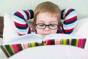 Image of a child reading in bed wearing glasses.