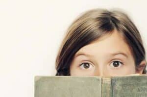 girl holds book up to face